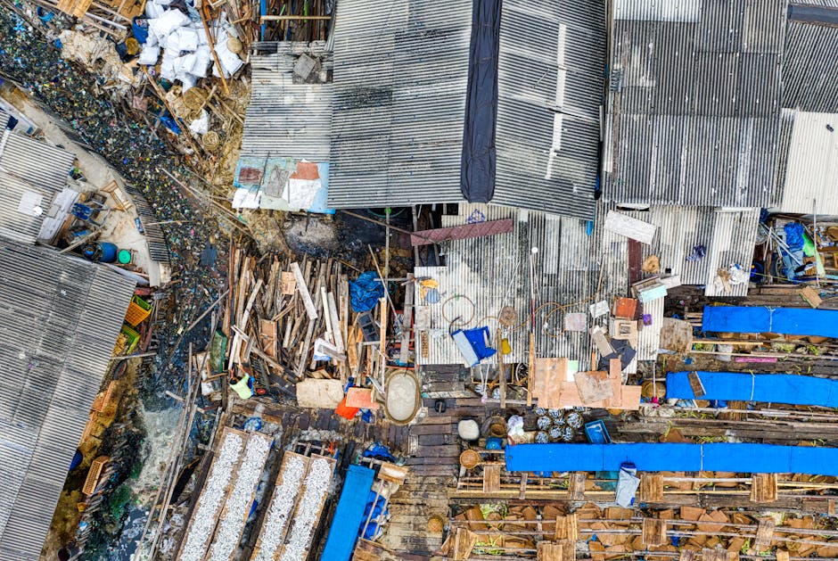 An aerial view of a cluttered area of makeshift structures and sheds constructed from corrugated metal sheets, with varying shades of silver and grey, some showing signs of rust and wear. The scene in